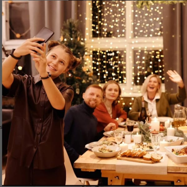 A young woman takes a selfie with friends and family at a festive dinner table.