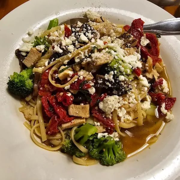 A close-up of a pasta dish with broccoli, sun-dried tomatoes, chicken, and feta cheese.