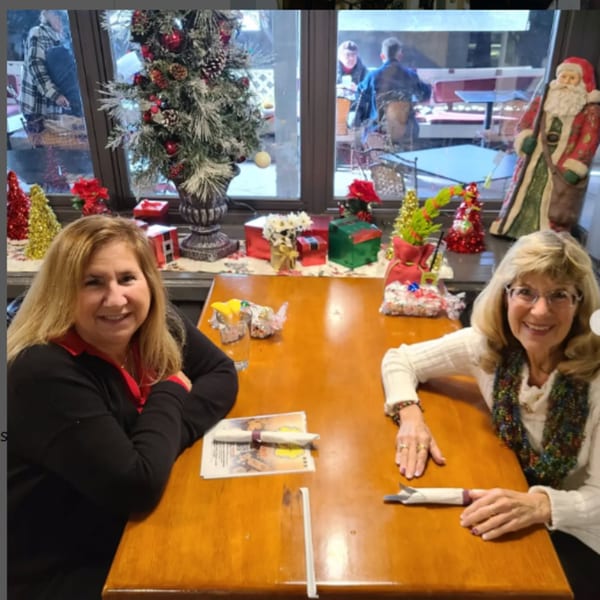 Two women smiling at a table in Misto Caffe & Bakery, decorated for Christmas.