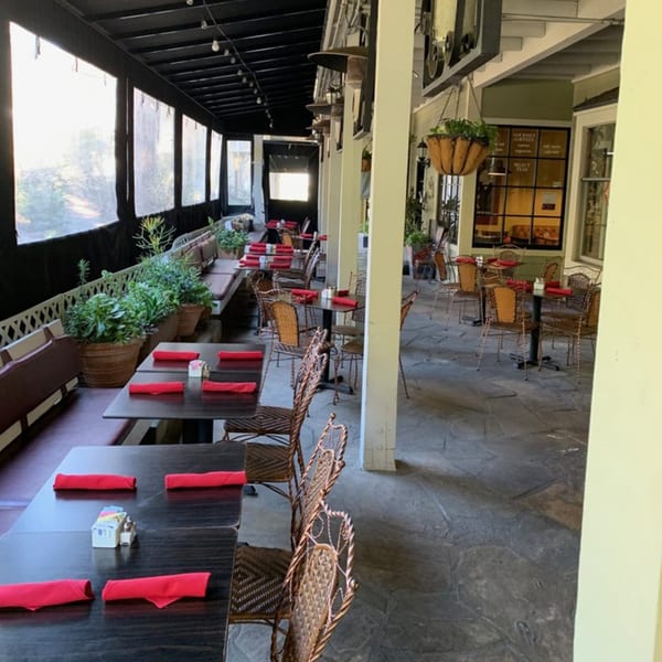 Outdoor patio dining area at Misto Caffe & Bakery with dark tables, red napkins, and potted plants.
