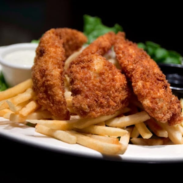 Crispy fried chicken tenders and golden french fries on a white plate with dipping sauce and lettuce.