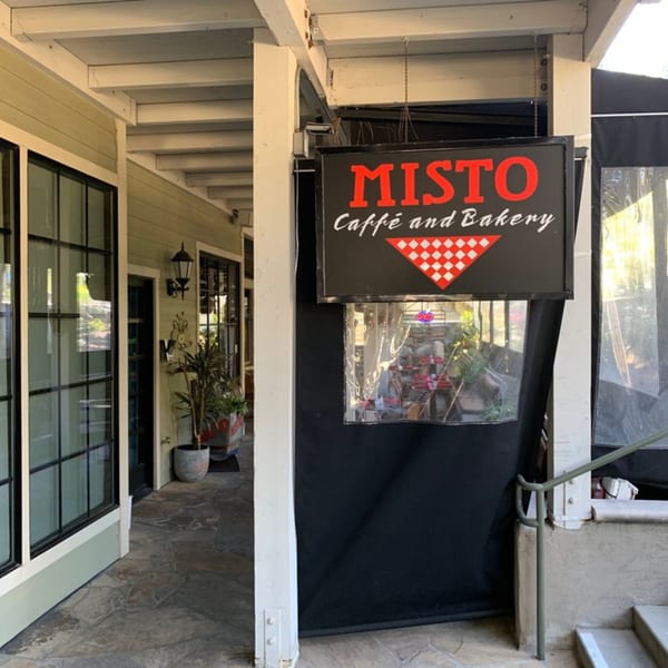 Misto Caffe and Bakery sign hanging outside the restaurant entrance with outdoor seating.