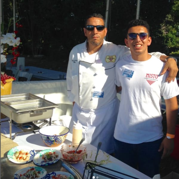 Two Misto Caffe & Bakery staff, one chef and one server, stand behind a food display.