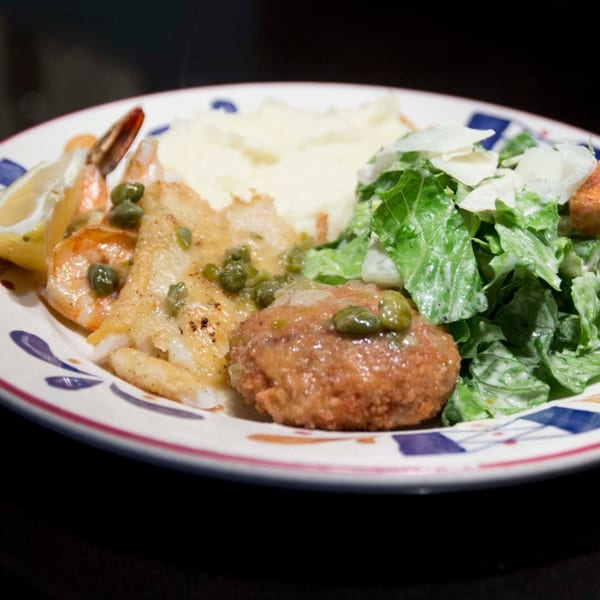 A plate with fish, shrimp, mashed potatoes, a crab cake, and a side salad.