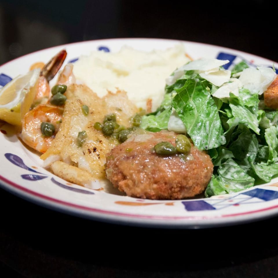 A plate with fish, shrimp, mashed potatoes, a crab cake, and a side salad.