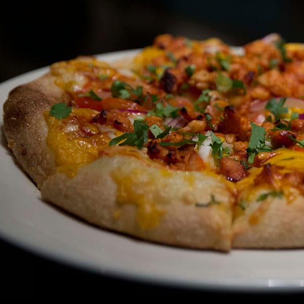 Close-up of a Misto Caffe & Bakery breakfast pizza with melted cheese, chicken, and herbs.