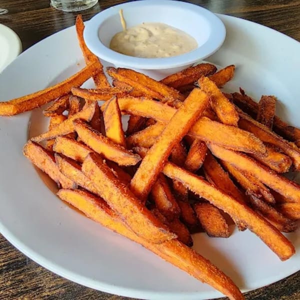 A white plate filled with crispy sweet potato fries and a small bowl of dipping sauce.