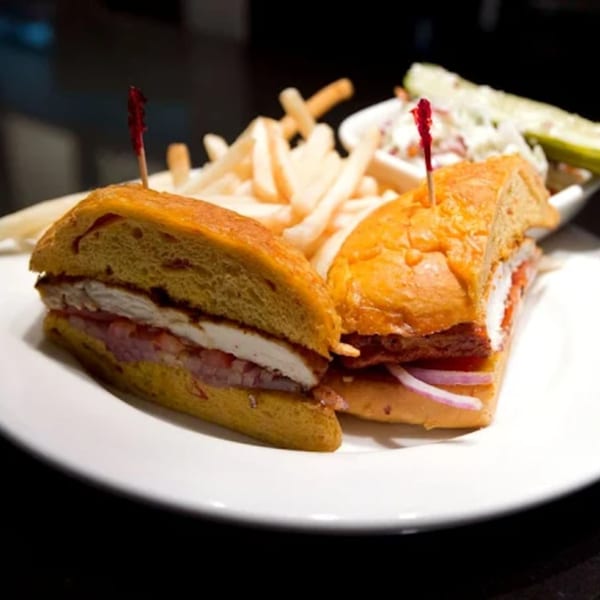 Two halves of a chicken sandwich with bacon, red onion, and tomato, served with fries and coleslaw.