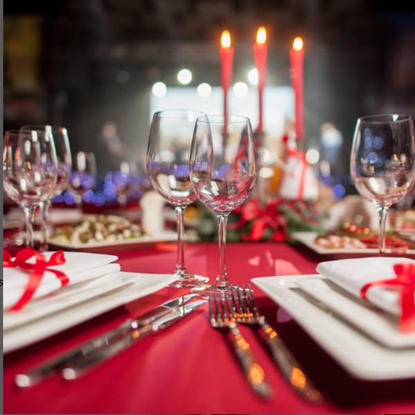 Elegant dining table set with red tablecloth, wine glasses, cutlery, and lit candles.