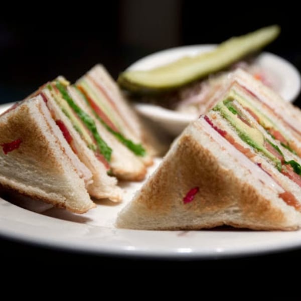 Club sandwich with avocado, tomato, and lettuce, served with a pickle spear.